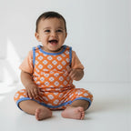 Baby wearing an orange outfit with white patterns on a white background