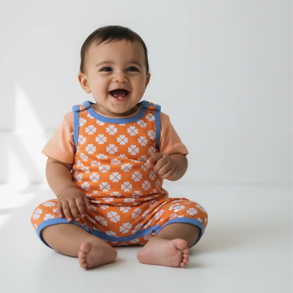 Baby wearing an orange outfit with white patterns on a white background