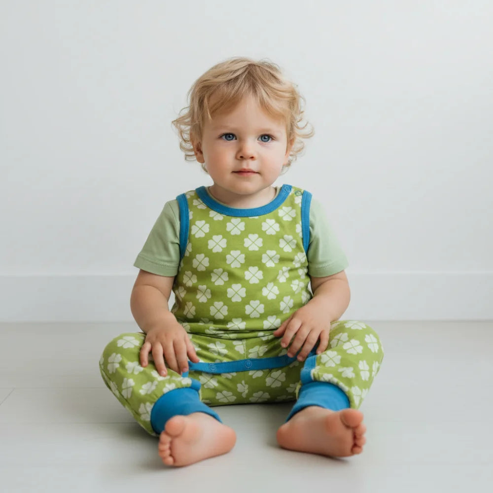 Baby wearing a green and blue outfit with clover pattern on a white background