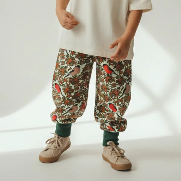 Child wearing floral-patterned pants with birds on a plain background