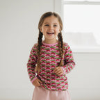 Young girl wearing a pink long-sleeve shirt with a strawberry pattern against a white background