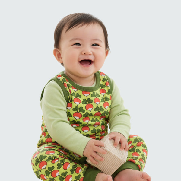 Baby wearing a green outfit with red patterns, sitting on a white background