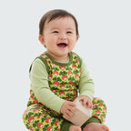 Baby wearing a green outfit with red patterns, sitting on a white background