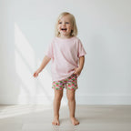 Child wearing a pink shirt and strawberry print shorts on a white background