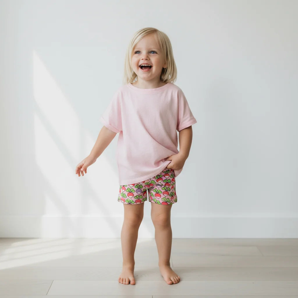 Child wearing a pink shirt and strawberry print shorts on a white background