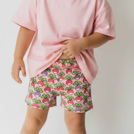 Child wearing a pink shirt and strawberry print shorts on a white background