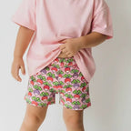 Child wearing a pink shirt and strawberry print shorts on a white background