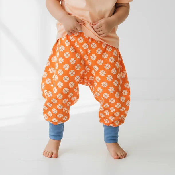 Child wearing a peach shirt and orange floral pants on a white background