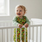 Child in a green shirt and yellow floral overalls standing in a crib.