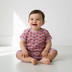 Baby wearing a pink outfit with strawberry pattern on a white background