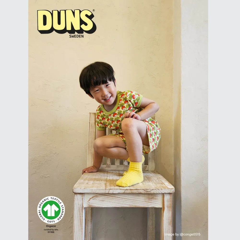 Child sitting on a wooden chair wearing a colorful outfit with Duns Sweden branding.