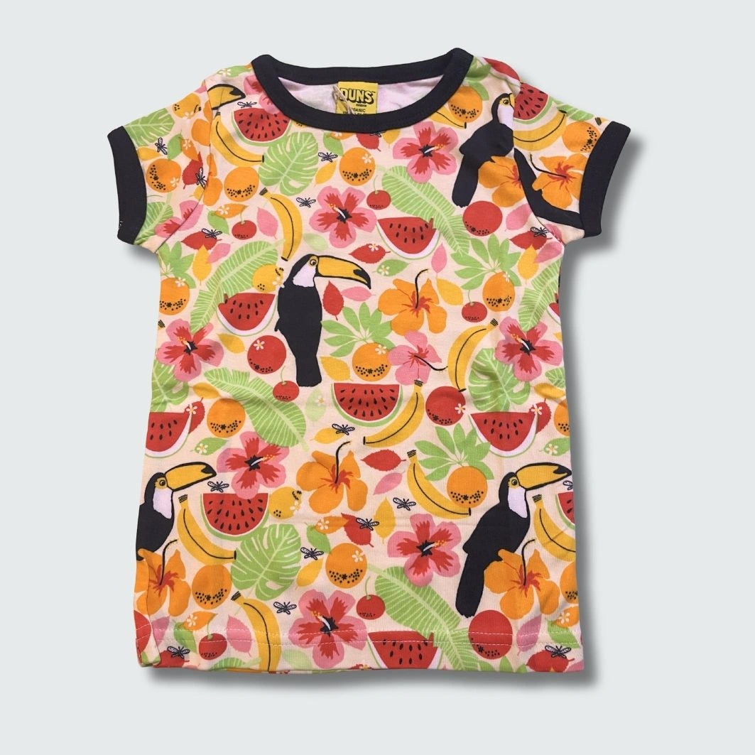 Front view of colorful t-shirt with tropical fruit and bird pattern on a light gray background