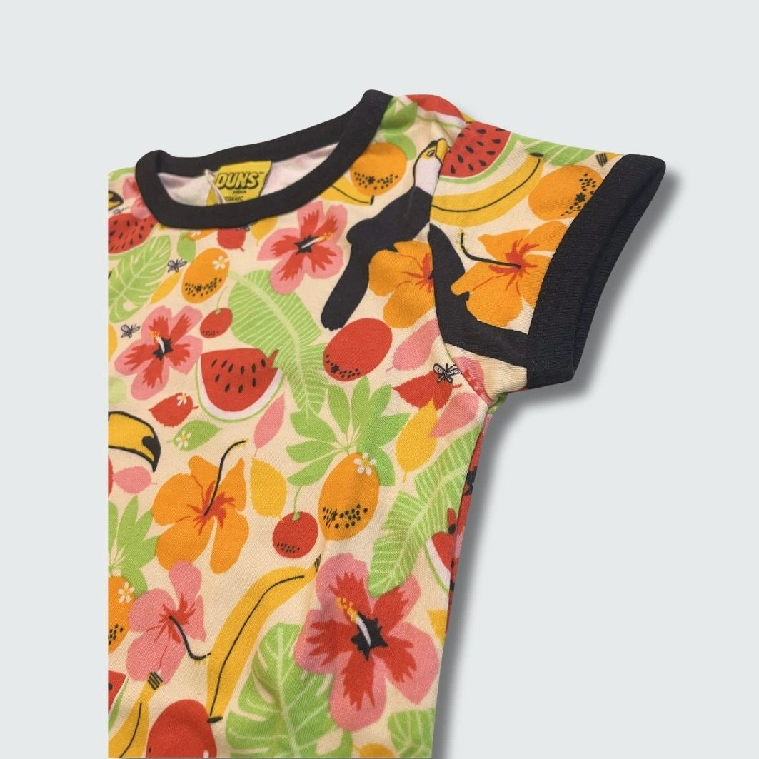 Close-up of colorful t-shirt with tropical fruit and bird pattern and black trim on a light gray background