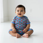 Baby wearing a blue onesie with red and green patterns on a white background