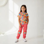 Young girl wearing a colorful patterned shirt and pink pants with heart designs on a white background