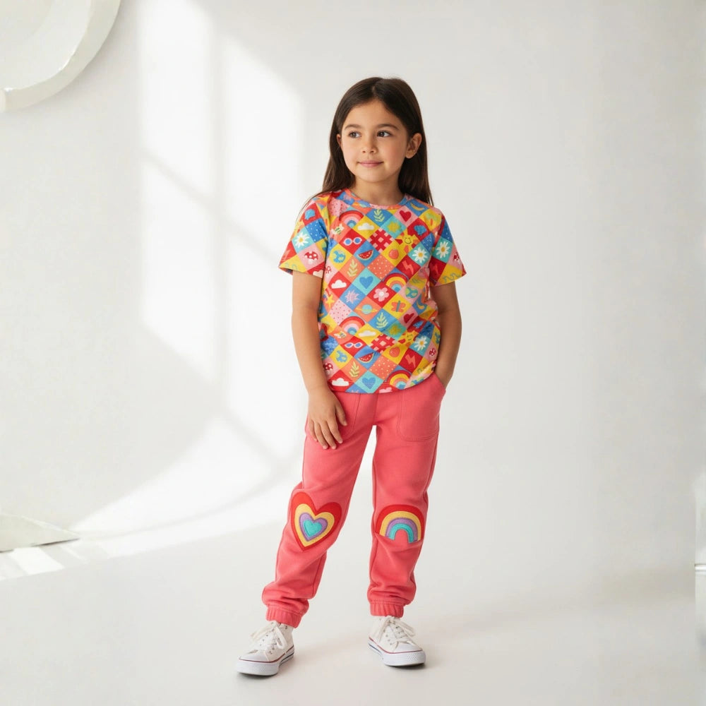 Young girl wearing a colorful patterned shirt and pink pants with heart designs on a white background