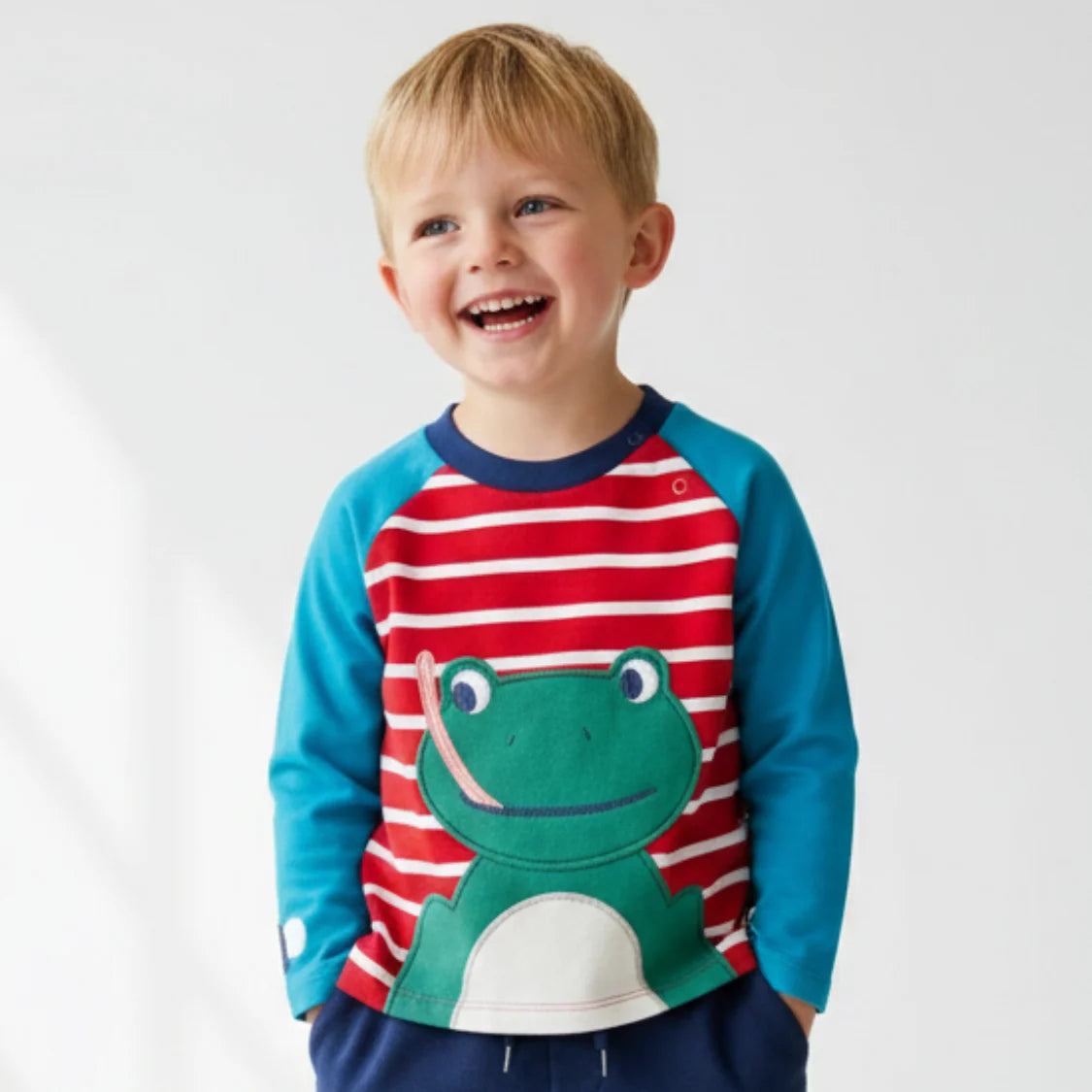 Child wearing a colorful shirt with a frog design on a plain background