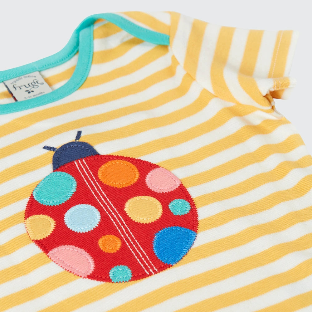 Yellow and white striped baby dress with a colorful ladybug patch on a white background