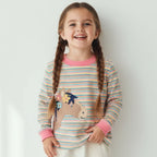 Young girl wearing a colorful striped shirt with a horse design on a plain background
