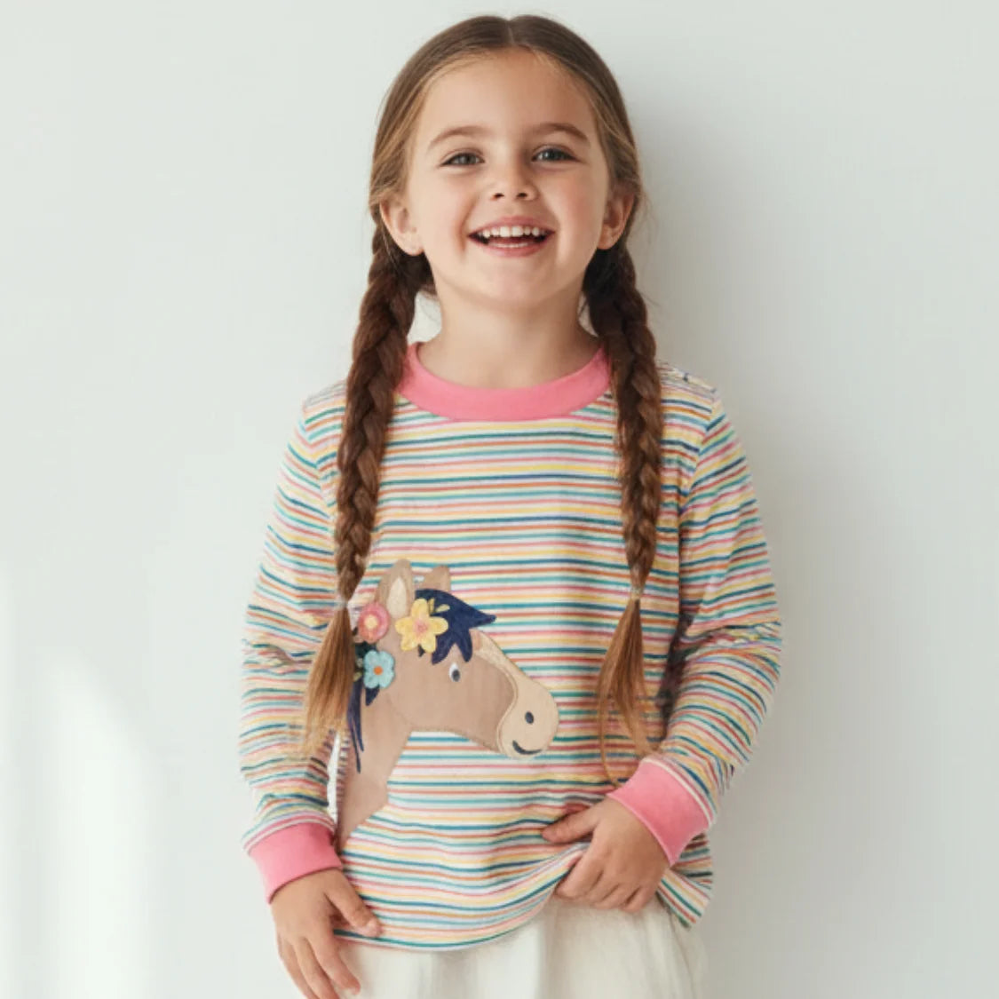 Young girl wearing a colorful striped shirt with a horse design on a plain background
