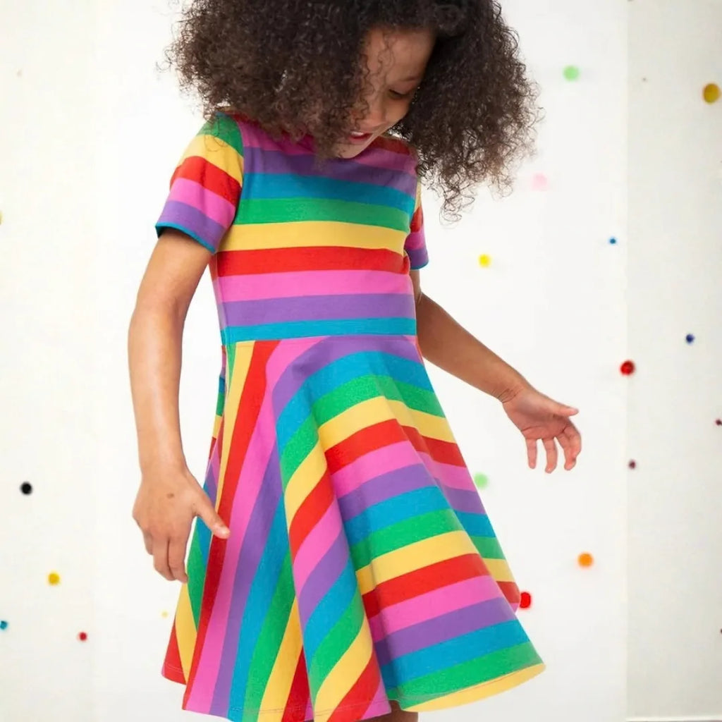 Girl twirling in the Frugi Sunshine Skater Dress, the rainbow striped circular skirt flaring out
