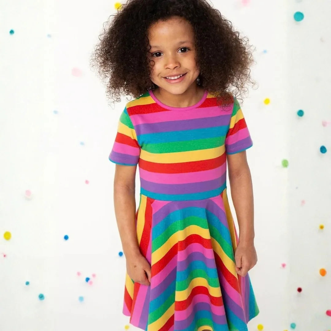 Smiling girl wearing the Frugi Sunshine Skater Dress in pink, purple, blue, green, yellow and red stripes