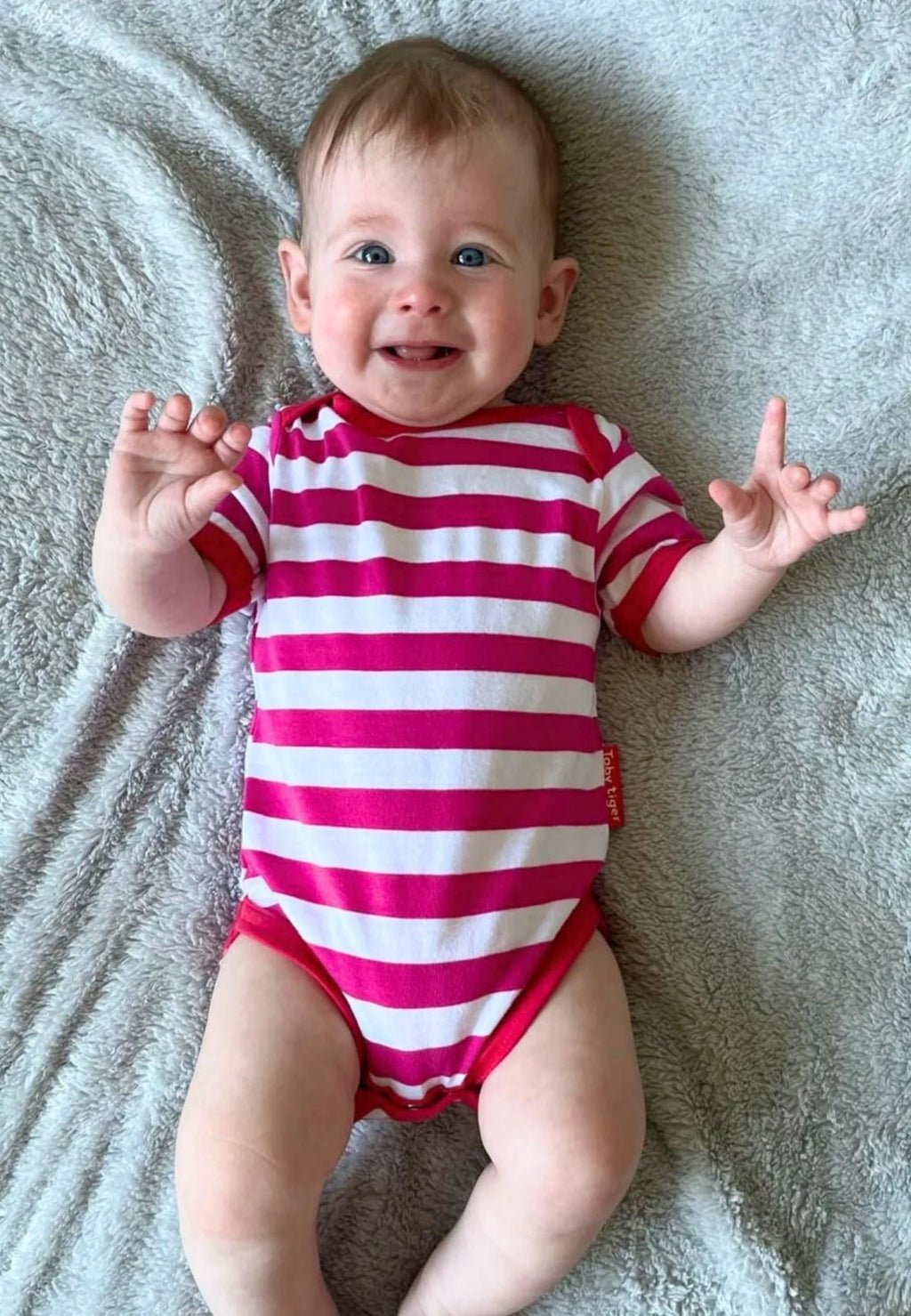 Baby wearing a red and white striped onesie on a gray blanket