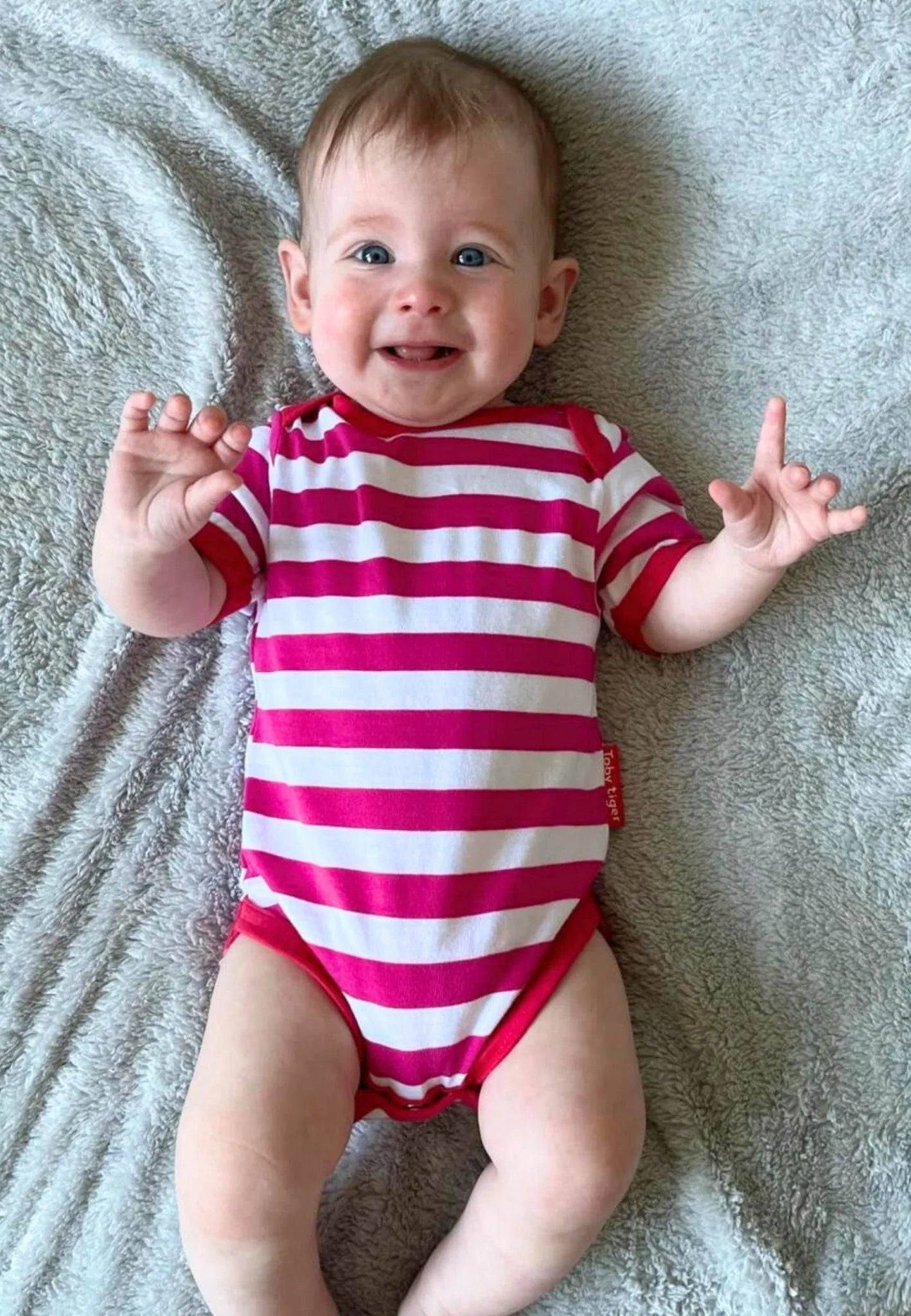 Baby wearing a red and white striped onesie on a gray blanket
