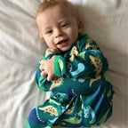 Baby wearing a dinosaur-themed onesie on a white blanket