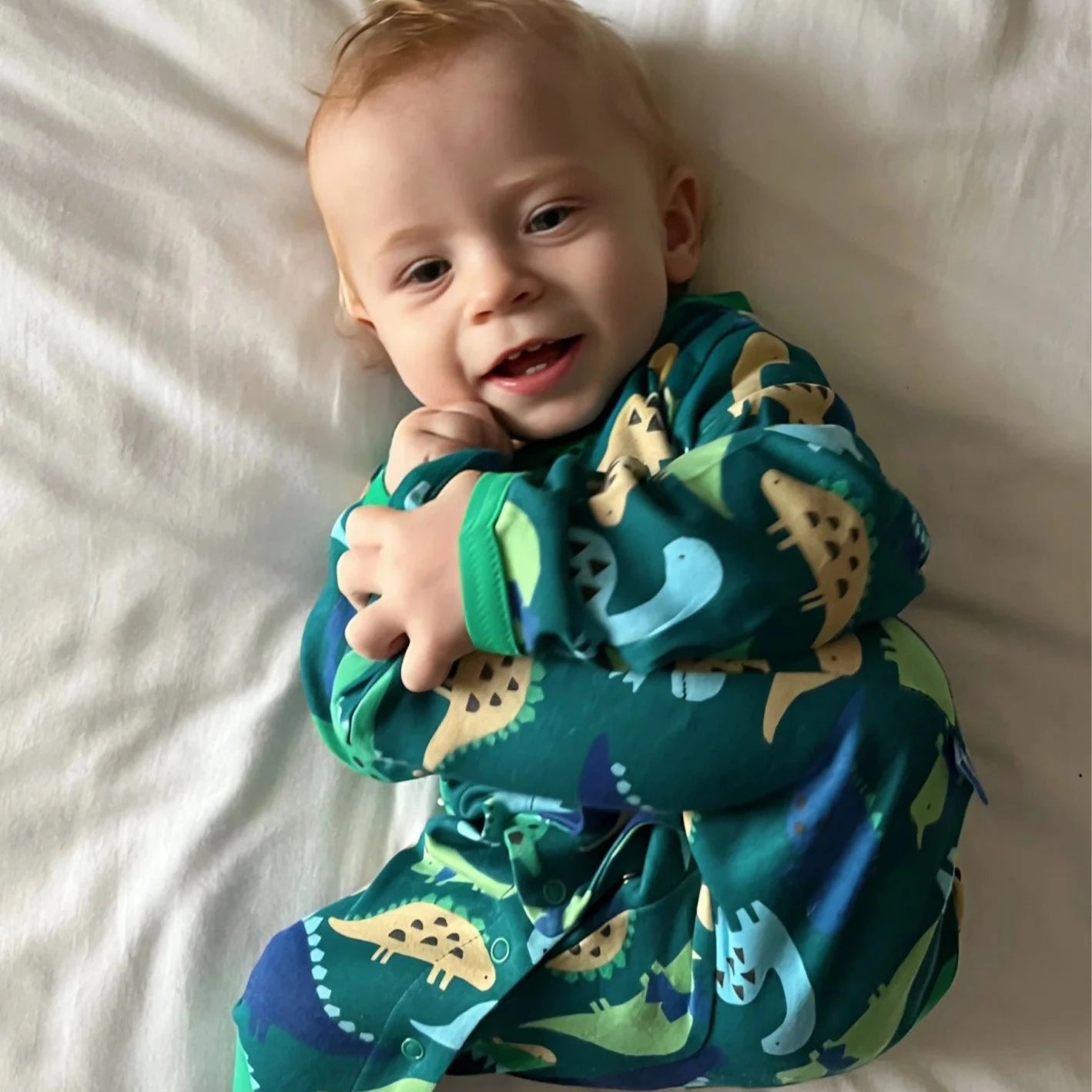 Baby wearing a dinosaur-themed onesie on a white blanket