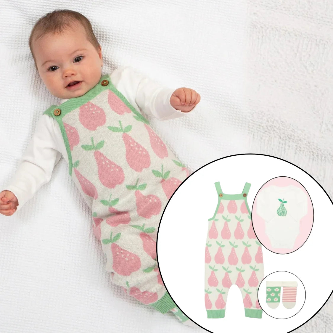 Baby wearing a pink and green romper with pear pattern, lying on a white blanket.