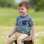 Child wearing a patterned shirt sitting outdoors on a grassy area