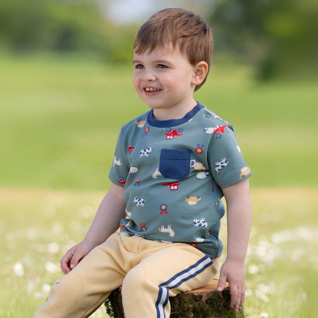 Child wearing a patterned shirt sitting outdoors on a grassy area