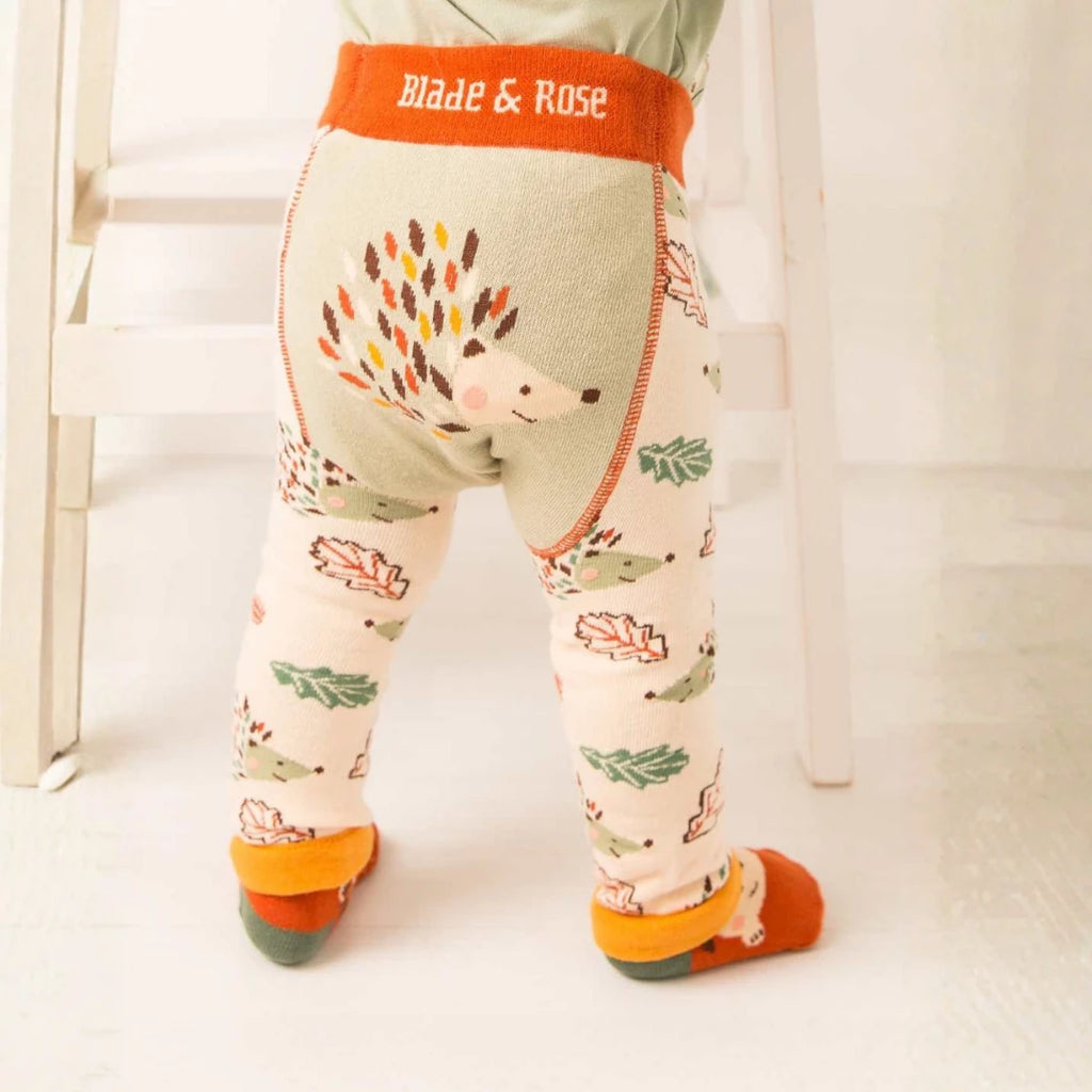 A child's lower body wearing patterned leggings with a hedgehog design and autumn leaves, featuring an orange waistband that reads 'Blade & Rose'.