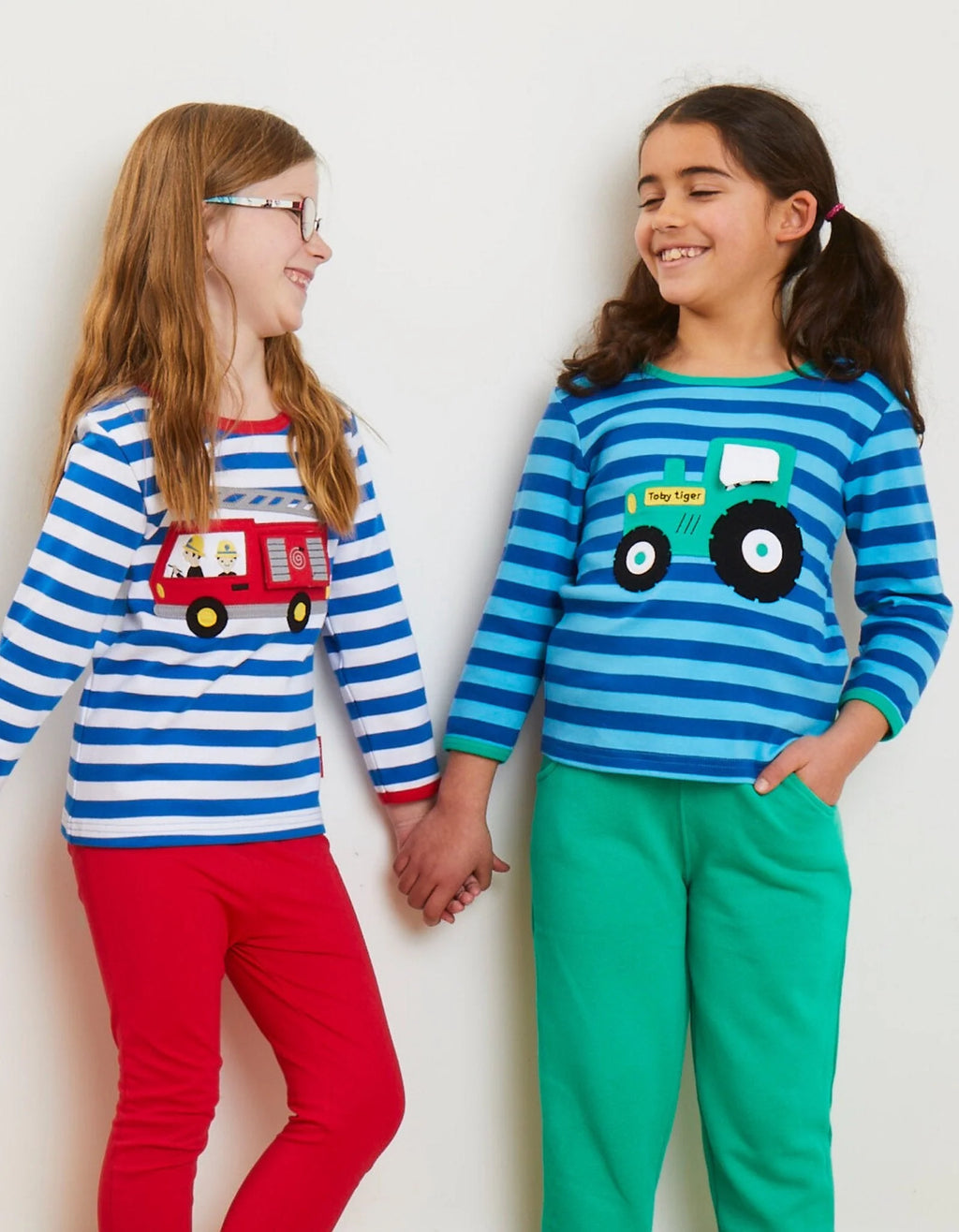 Two children wearing matching striped shirts with vehicle designs on a plain background