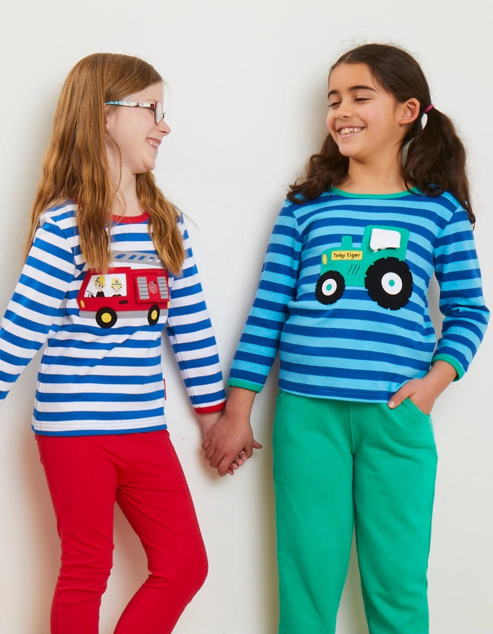 Two children wearing matching striped shirts with vehicle designs on a plain background