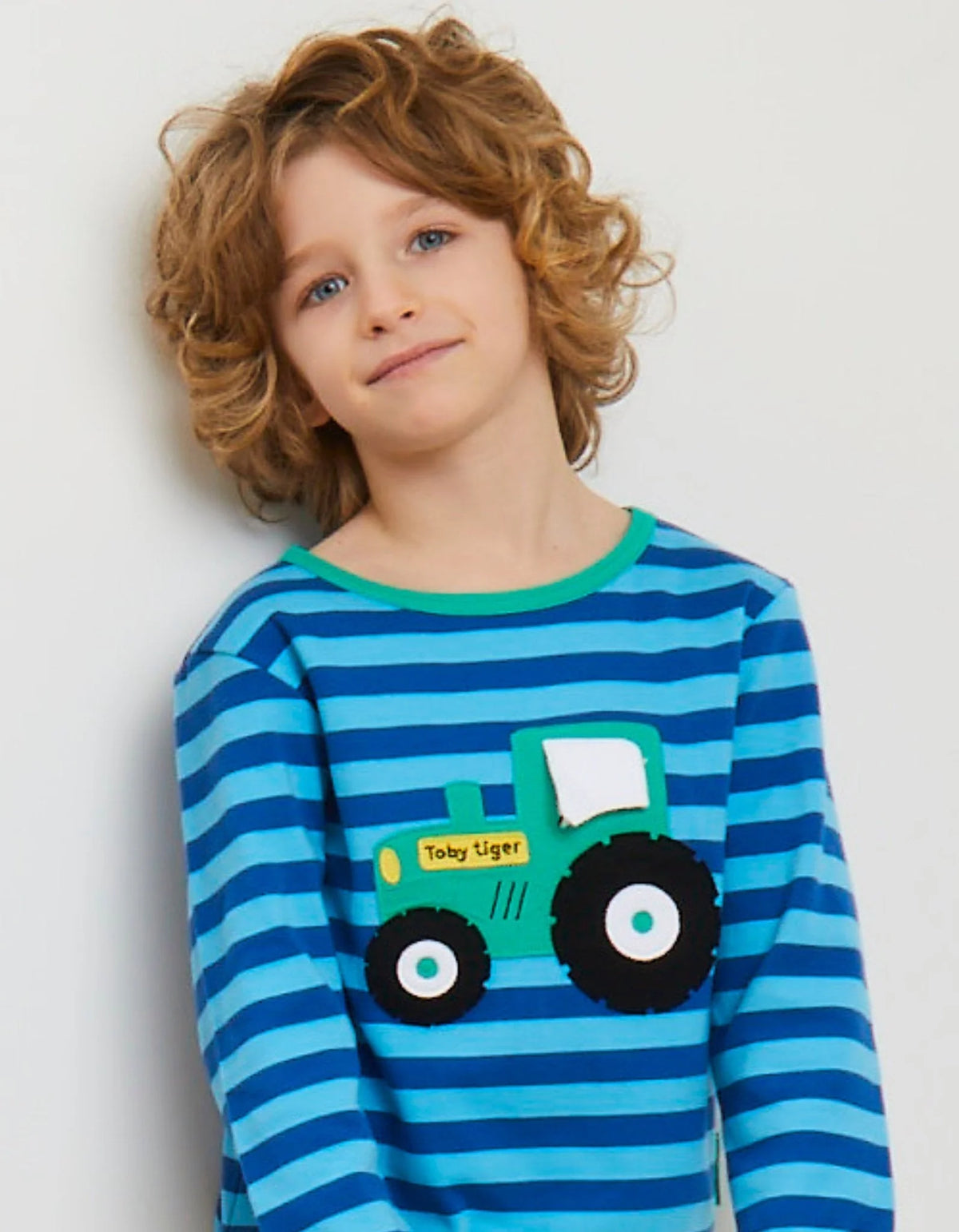 Child wearing a blue striped shirt with a green tractor design on a white background