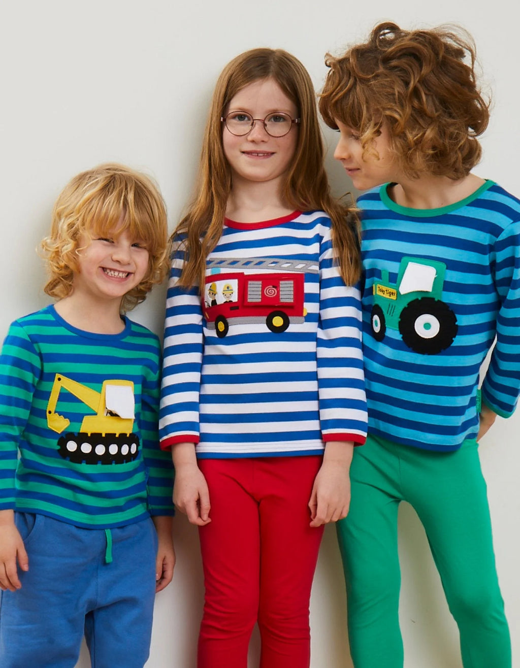 Three children wearing colorful pajamas with vehicle designs on a plain background