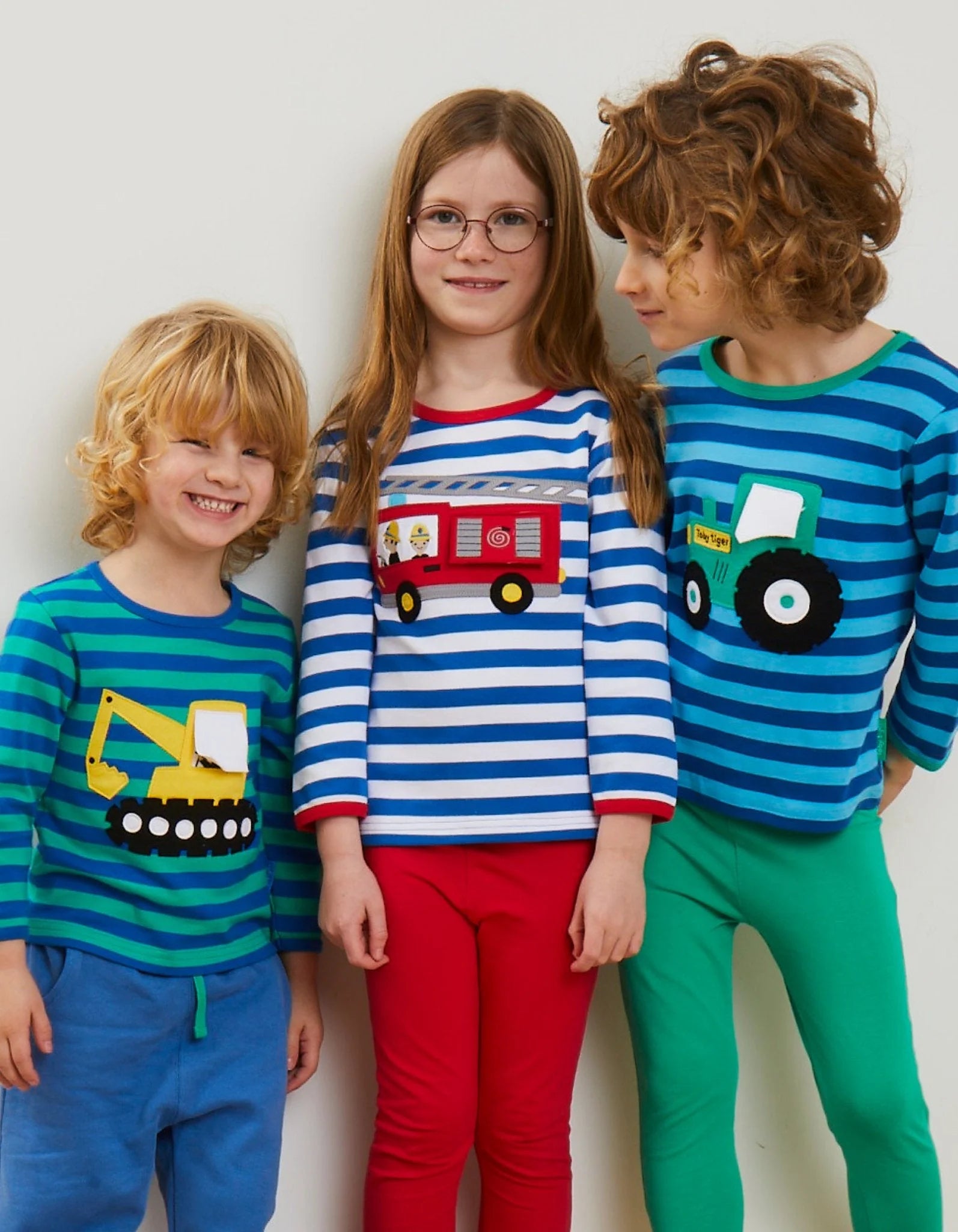 Three children wearing colorful pajamas with vehicle designs on a plain background