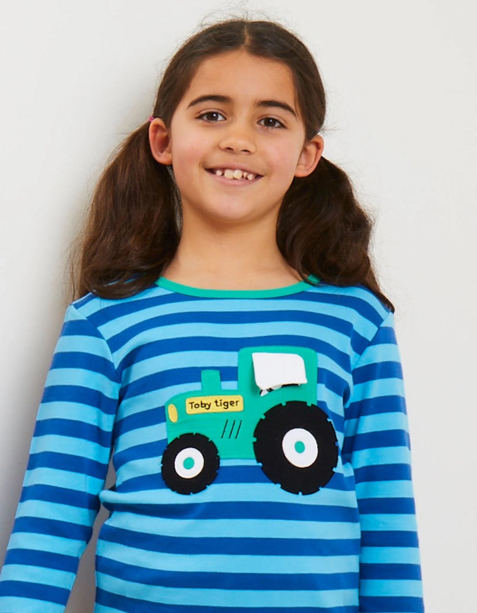Young girl wearing a blue striped shirt with a toy tiger design on a white background