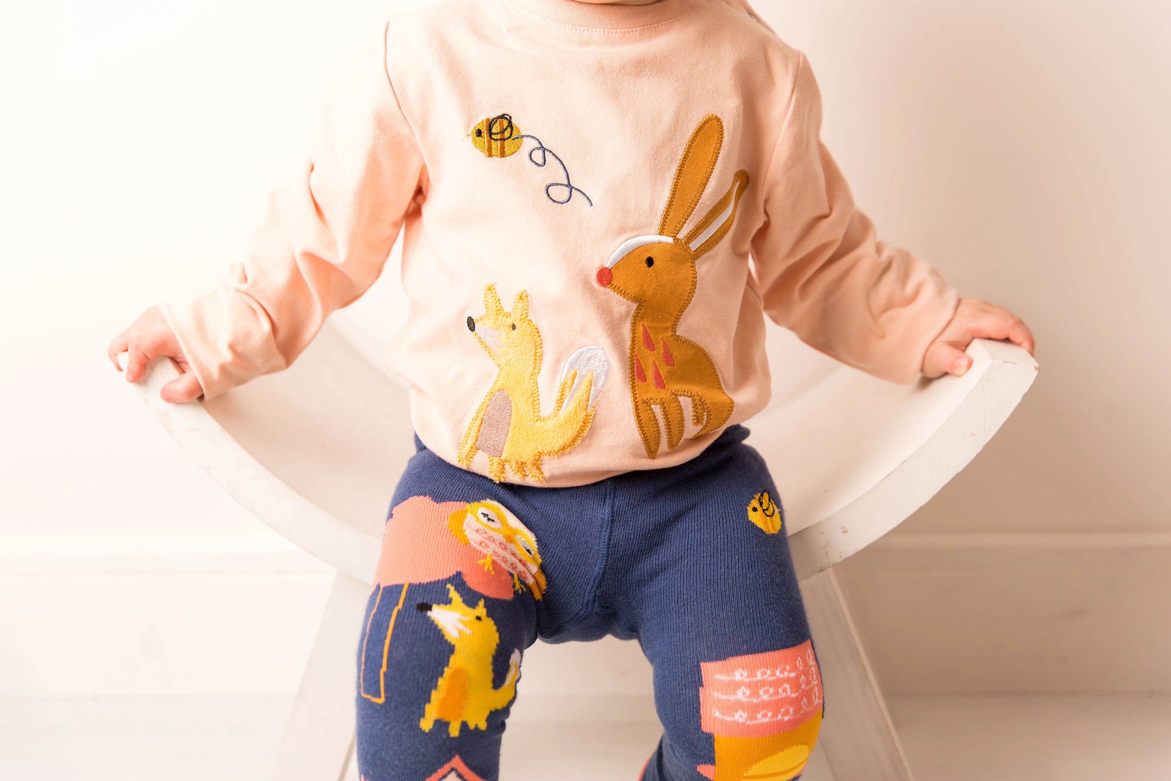 Child wearing a light pink shirt with animal graphics and dark blue pants with colorful patterns on a white background
