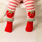 A close-up of a child's legs wearing red and pink striped tights with embroidered smiling strawberries near the cuffs, paired with bright red socks that also have a smiling face.