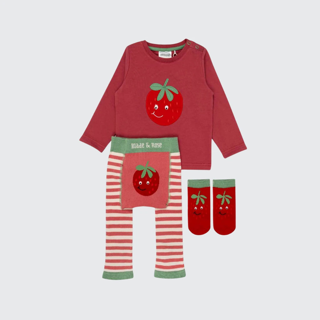 A children's three-piece pajama set laid flat on a light gray background. The set includes a long-sleeve red top with a smiling red strawberry graphic on the chest, matching red and white striped leggings with a red strawberry graphic on the waistband, and a pair of red socks with green cuffs and a red strawberry graphic.