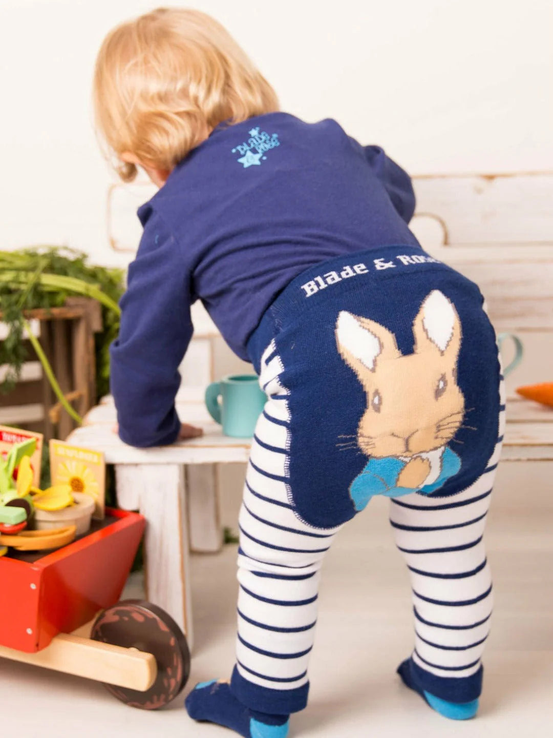 Child wearing a navy blue outfit with a rabbit design, standing on a white surface with toys around.