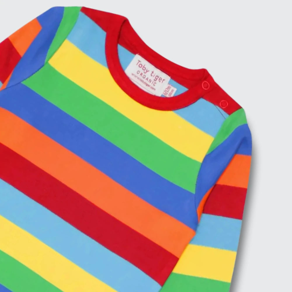 A close-up of a long-sleeve baby top with horizontal rainbow stripes in red, orange, yellow, green, light blue, and dark blue, featuring a red crew neck and a visible 'TooLoud' brand label.