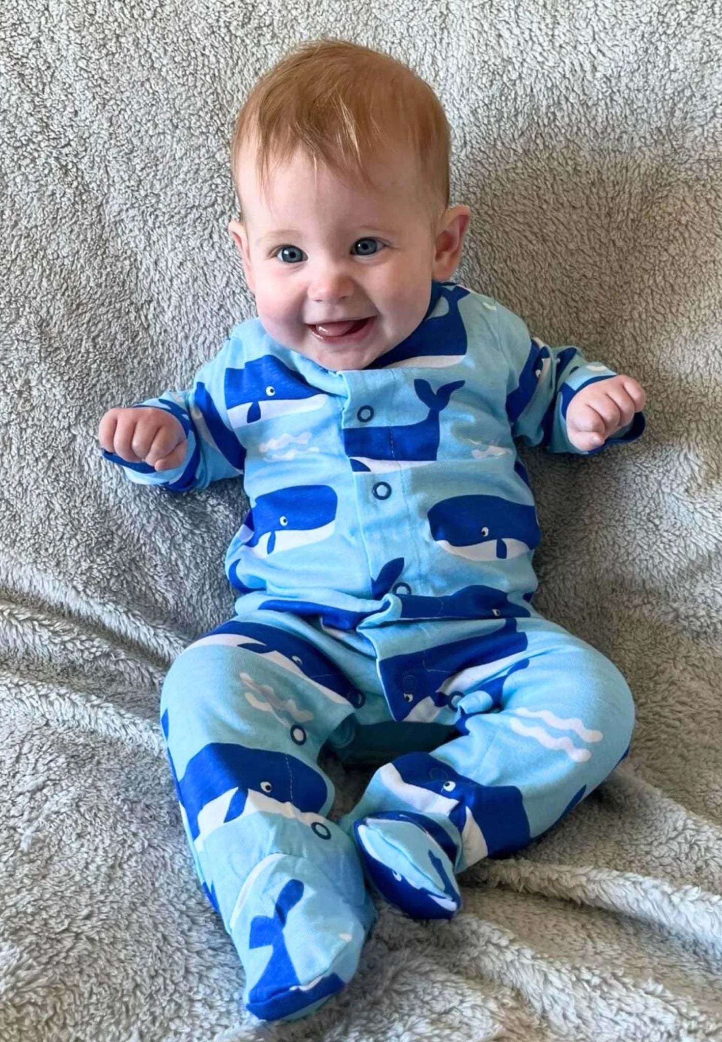 Baby wearing a blue onesie with whale patterns on a textured surface
