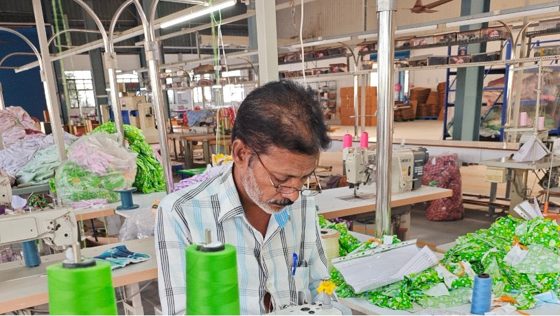 Man working at a sewing machine in a busy factory setting