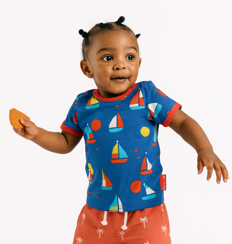 Child wearing a blue shirt with sailboat pattern and orange shorts on a white background