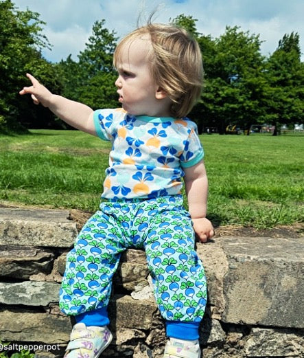 Child wearing a colorful outfit with floral patterns sitting on a stone wall in a park.