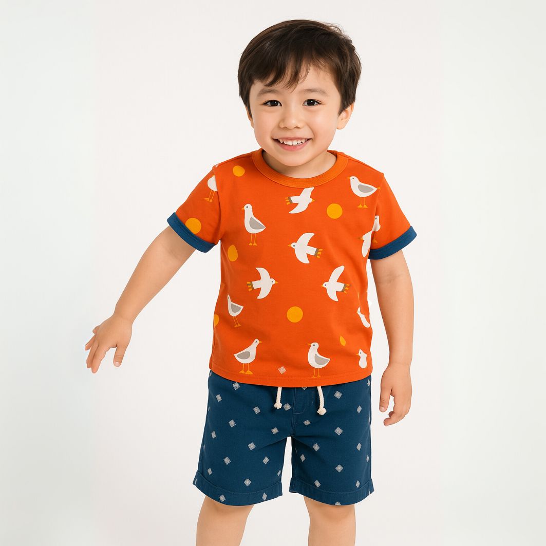 Child wearing an orange shirt with bird pattern and blue shorts on a white background